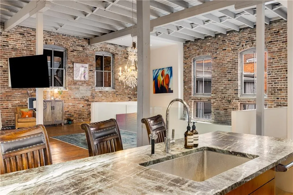 Kitchen featuring beam ceiling, wood finished floors, dark stone countertops, brick wall, and brown cabinets