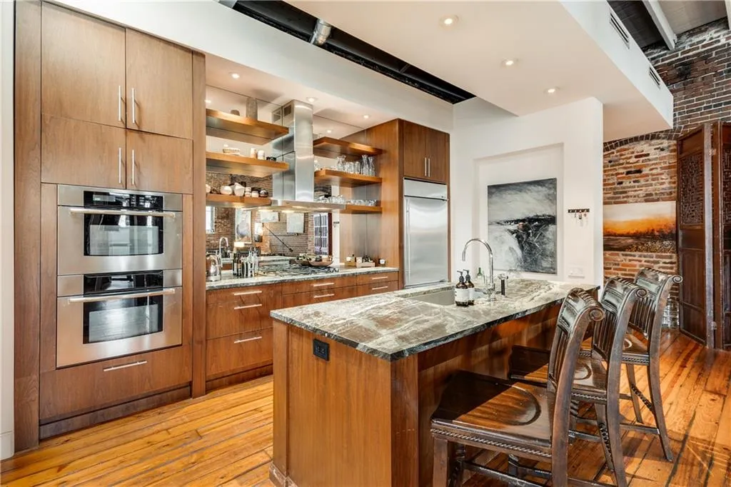 Kitchen featuring dark stone counters, open shelves, light wood finished floors, a breakfast bar area, and brick wall