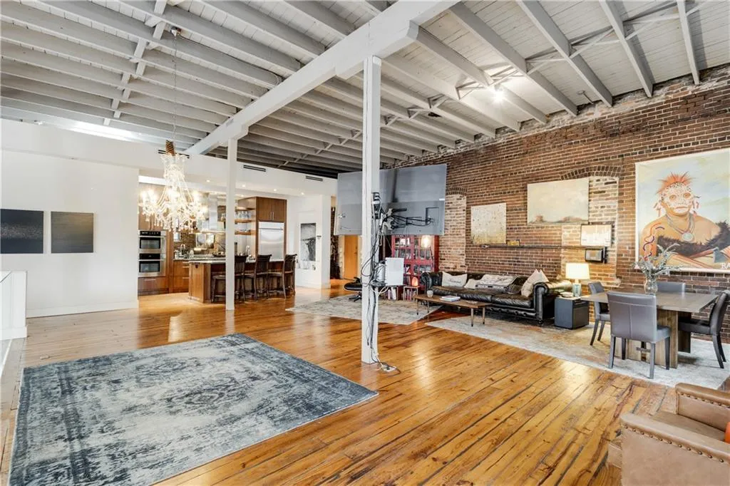Living area with brick wall, light wood finished floors, beam ceiling, and a high ceiling