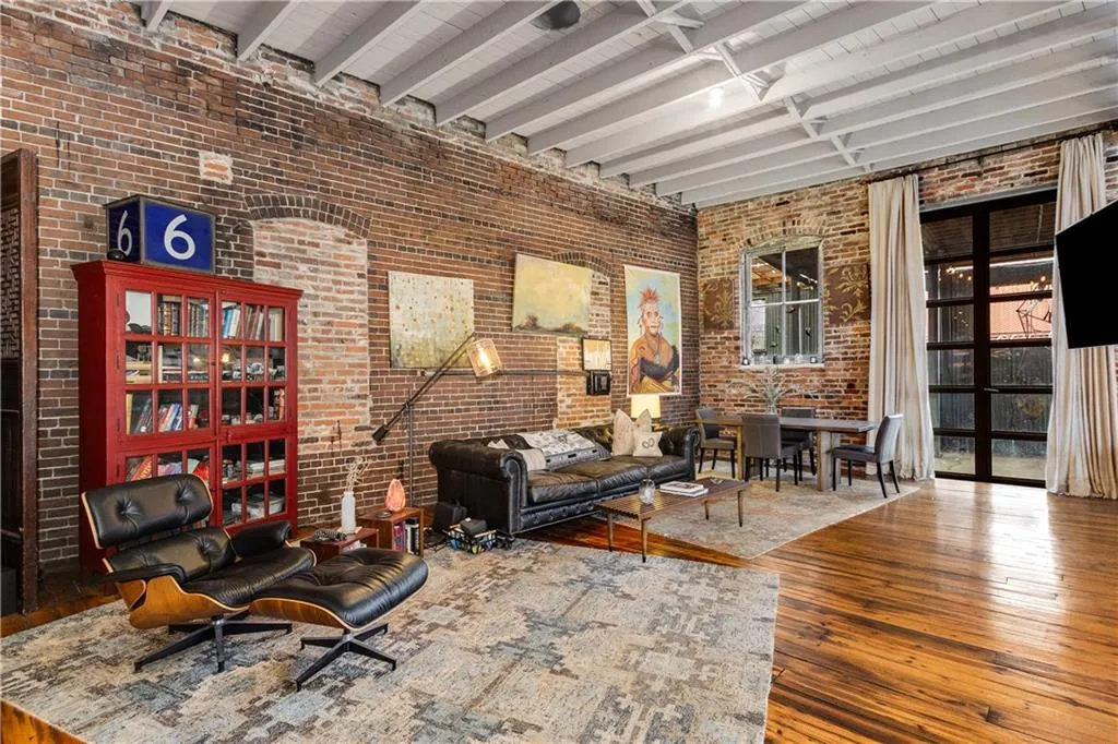 Living area with brick wall, beamed ceiling, hardwood / wood-style floors, and a high ceiling
