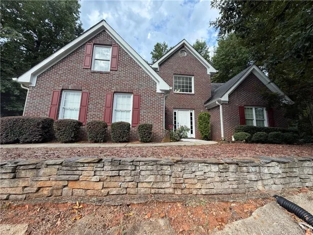 Brick exterior with contrasting red shutters, multiple gables, and a stone retaining wall