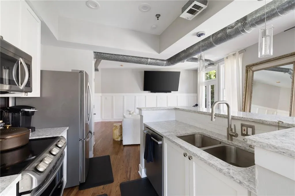 Kitchen with appliances with stainless steel finishes, white cabinets, light stone counters, wainscoting, and dark wood finished floors