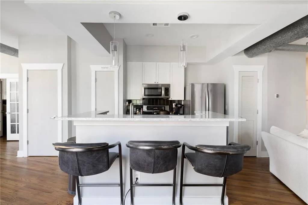 Kitchen featuring stainless steel appliances, a kitchen bar, dark wood finished floors, white cabinets, and hanging light fixtures