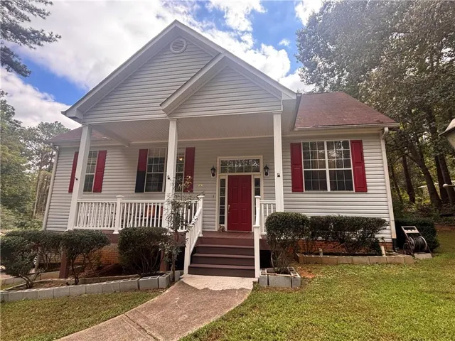 Gable roofline with red shingles, light gray siding, covered front porch, white railing, and a red front door