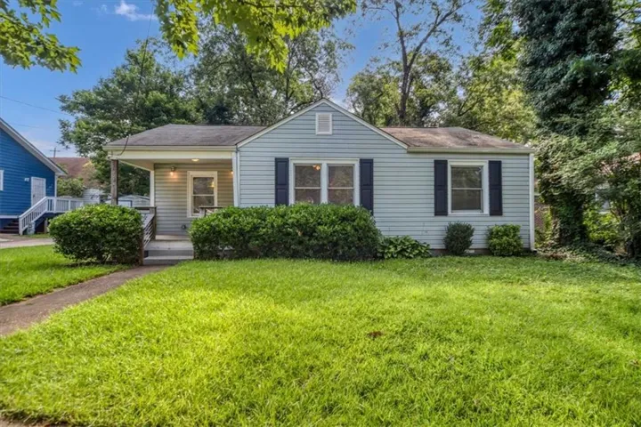 Classic cottage-style home featuring horizontal siding exterior, a covered front porch with supporting columns, black shutters framing multi-pane windows, and a brick walkway leading to the entrance