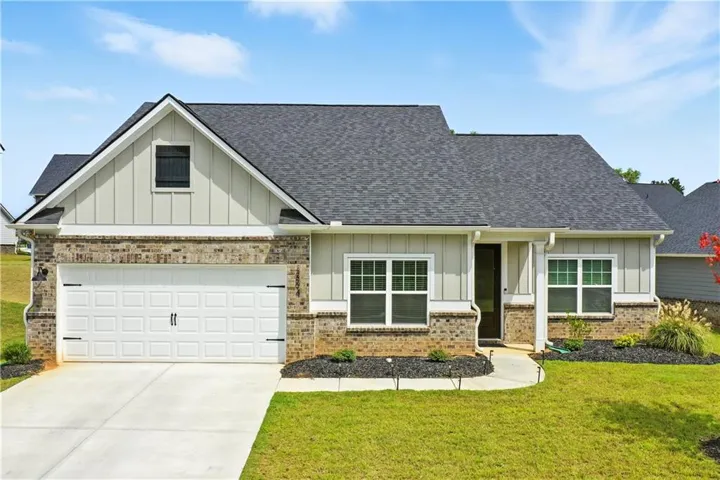 Craftsman-style home featuring board and batten siding, a front lawn, driveway, a garage, and roof with shingles