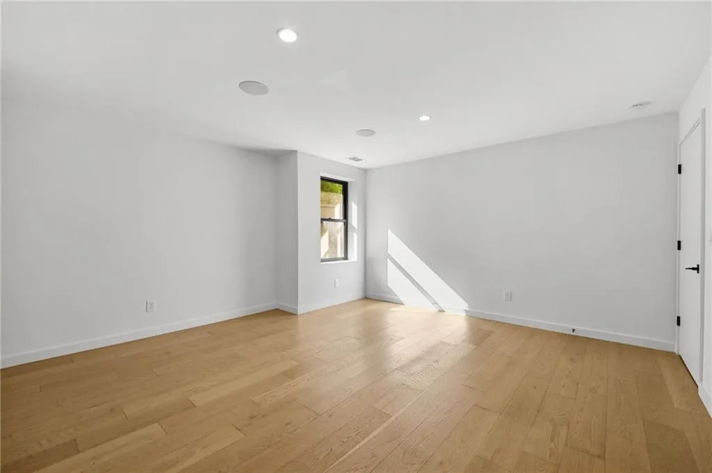 Spacious room featuring wood-finish flooring, recessed lighting, a black-framed window, and a white door with black hardware