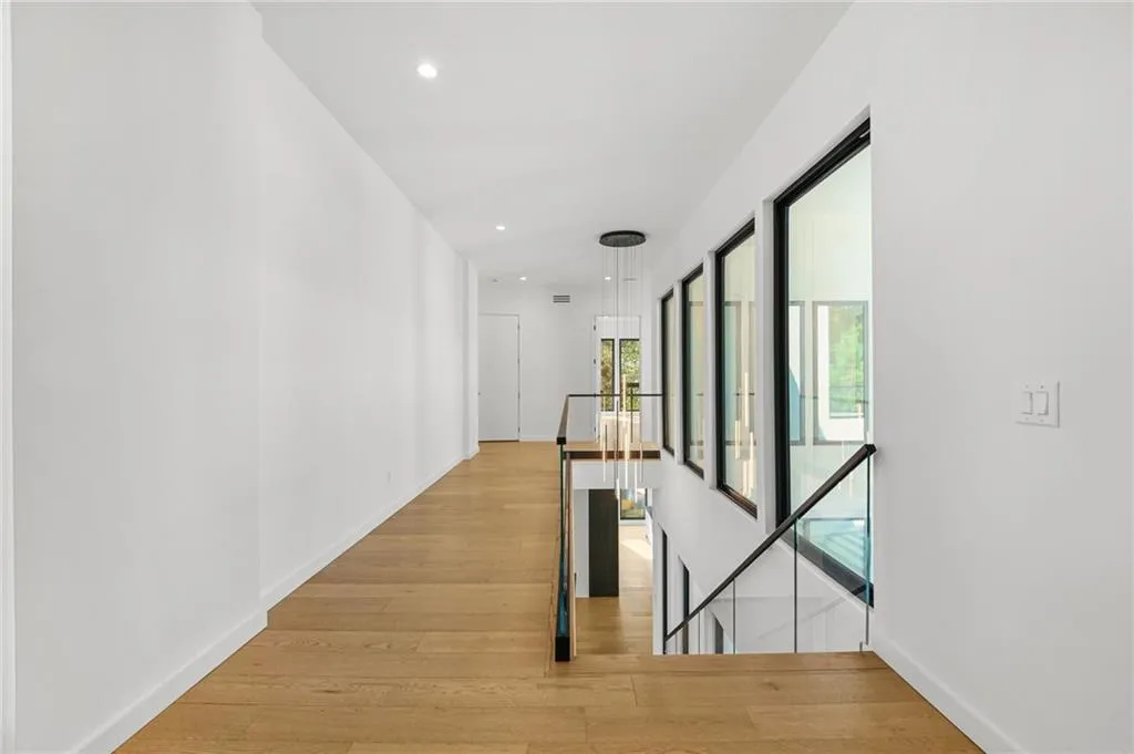 Recessed lighting, wood-finish flooring, glass panel railing, contemporary chandelier, and large windows with dark frames