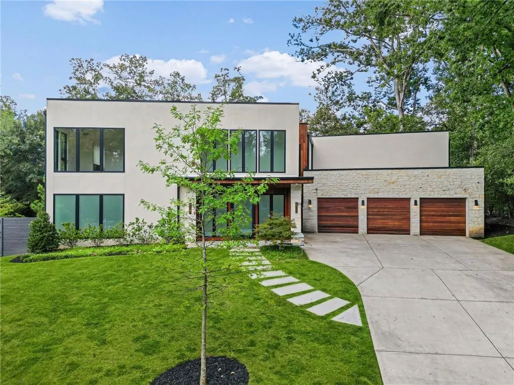 Contemporary exterior with a white stucco facade, stone accents, multiple large windows, a three-car garage with wood-finish doors, and a concrete driveway
