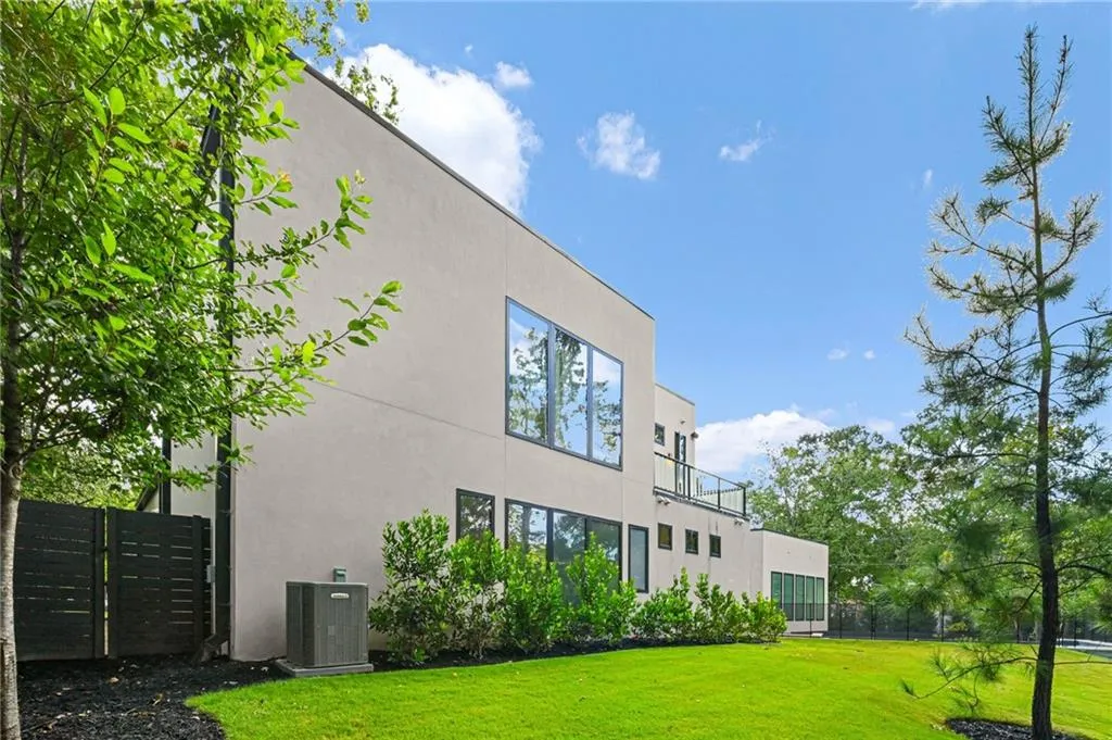 Modern stucco exterior with large windows, glass-paneled balcony, and a green lawn