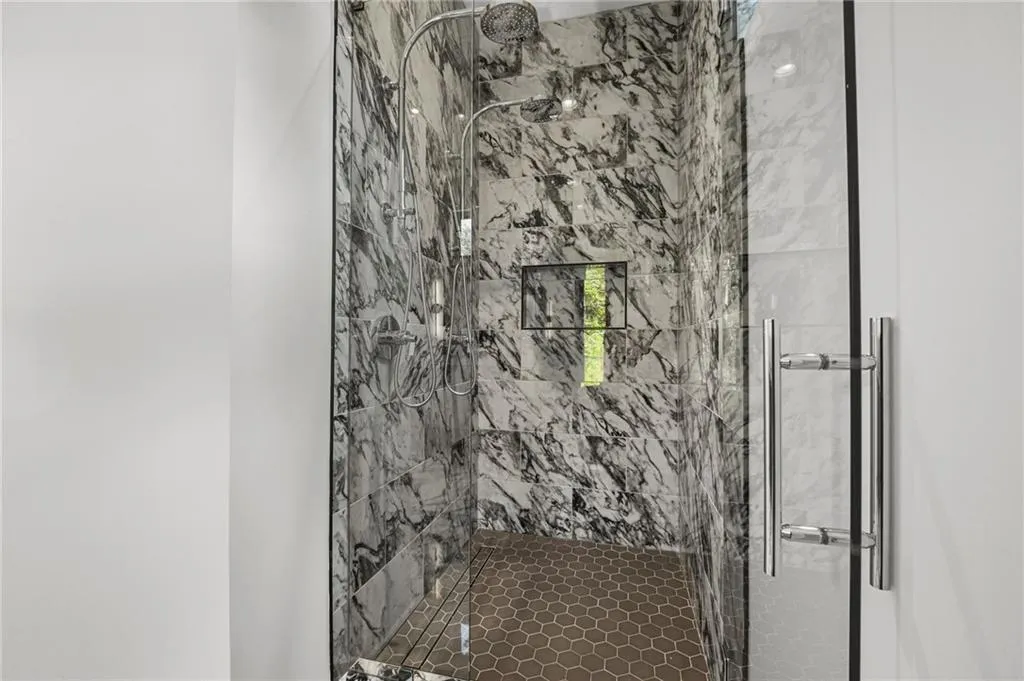 Walk-in shower with full-height marble-finish tile, glass enclosure, recessed shower niche, and hexagon floor tiling
