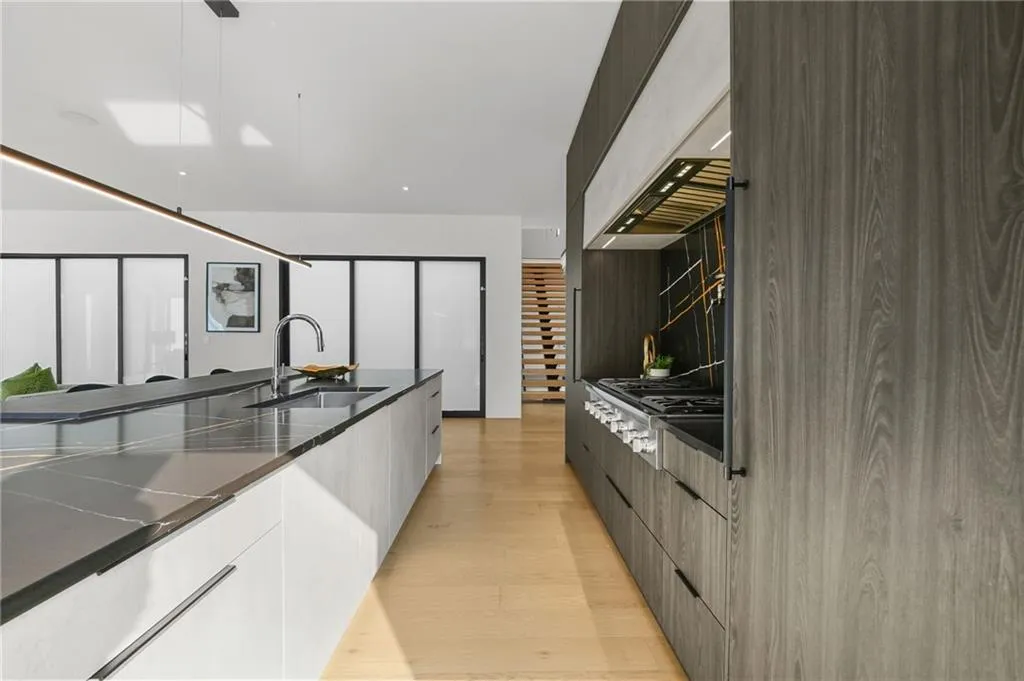 Modern kitchen featuring a large island with integrated sink, sleek wood-finish cabinetry, a professional-grade range, and light wood-finish flooring