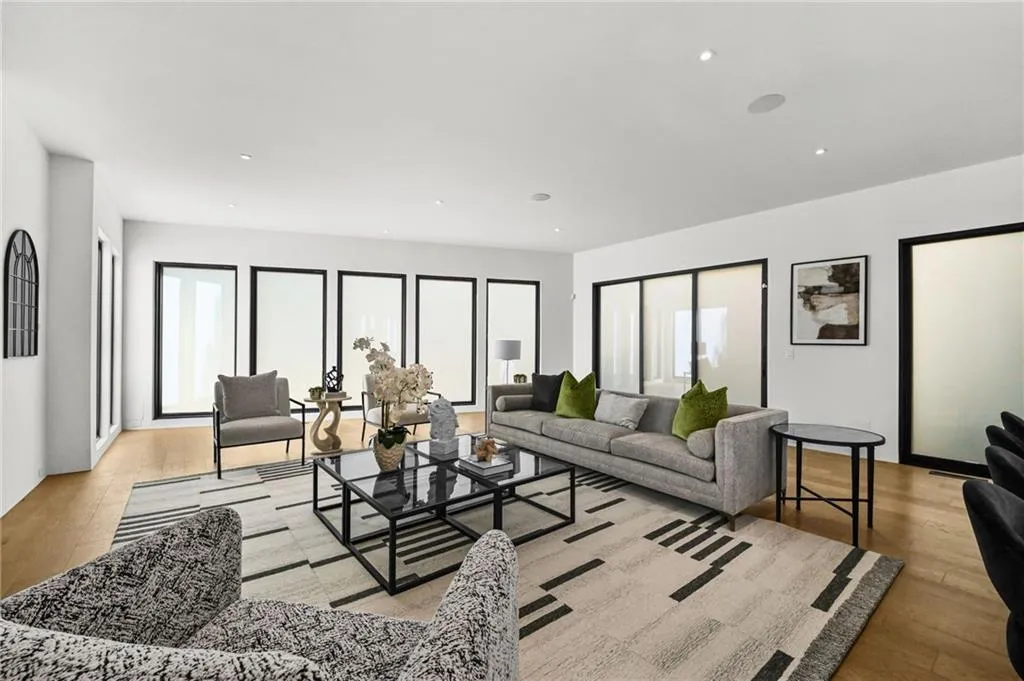 Recessed lighting illuminates wood-finish flooring and multiple floor-to-ceiling windows