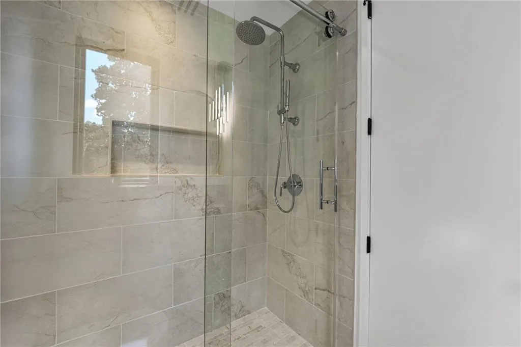 Glass-enclosed shower with a rainfall showerhead, handheld sprayer, and built-in niche
