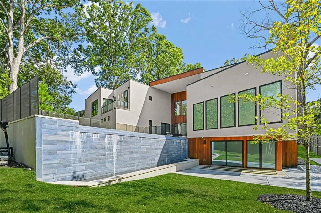 Contemporary exterior with multiple large windows, wood paneling accents, light-colored stucco, a stone-clad water feature, and well-maintained lawn