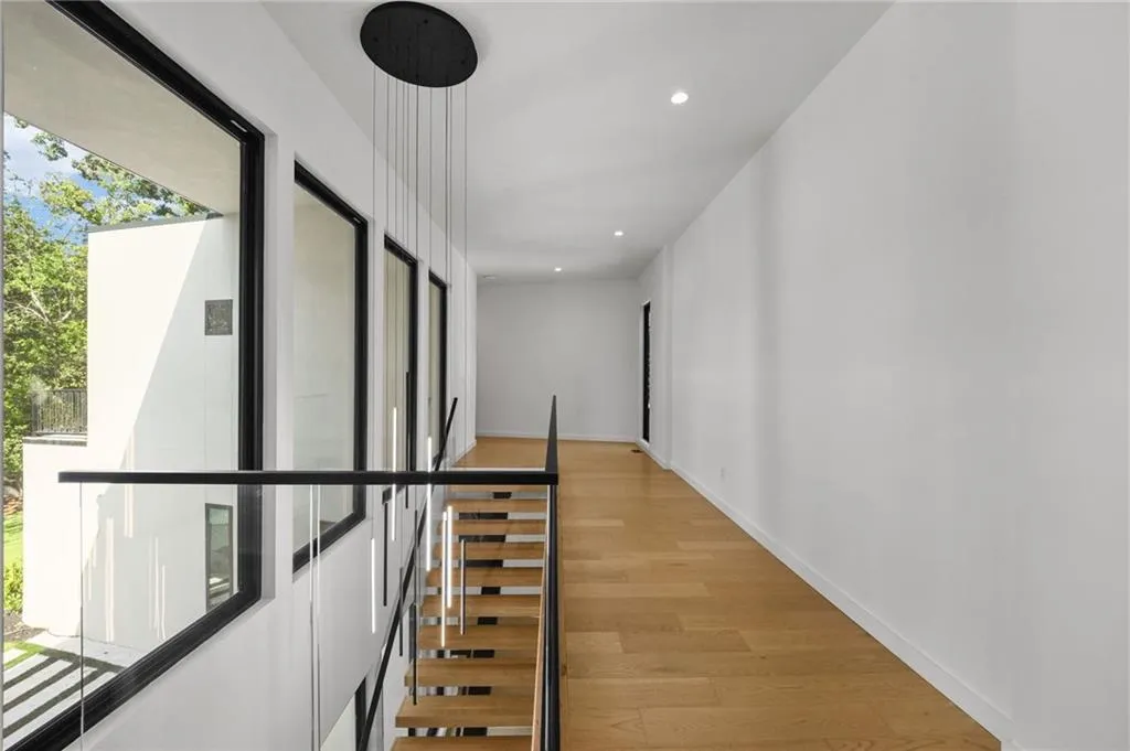 Hardwood flooring, recessed lighting, modern chandelier, glass panel railing, and large windows with black frames