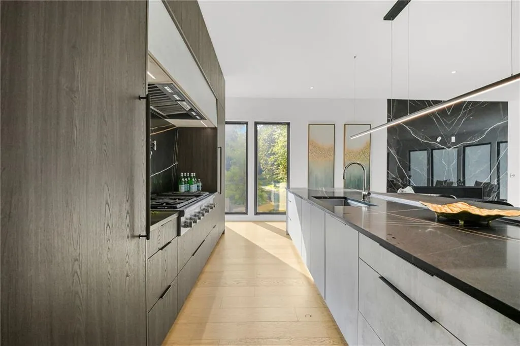 Gourmet kitchen featuring a professional-grade range, dark wood-finish cabinetry, a large center island with a sink, light wood-finish flooring, and expansive windows