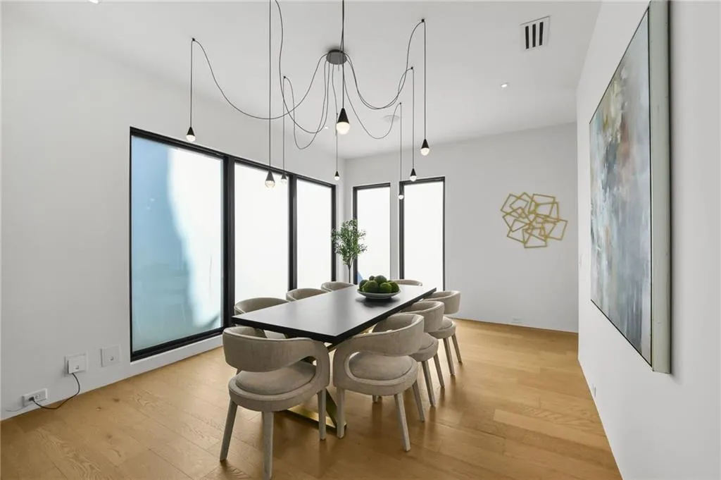 Clean lines and hardwood flooring frame this open concept space, featuring large windows and a multi-bulb ceiling fixture
