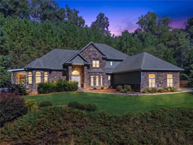 Elegant brick and stone exterior with multiple gables and a steep pitched roof, complemented by professional landscape lighting that illuminates the façade