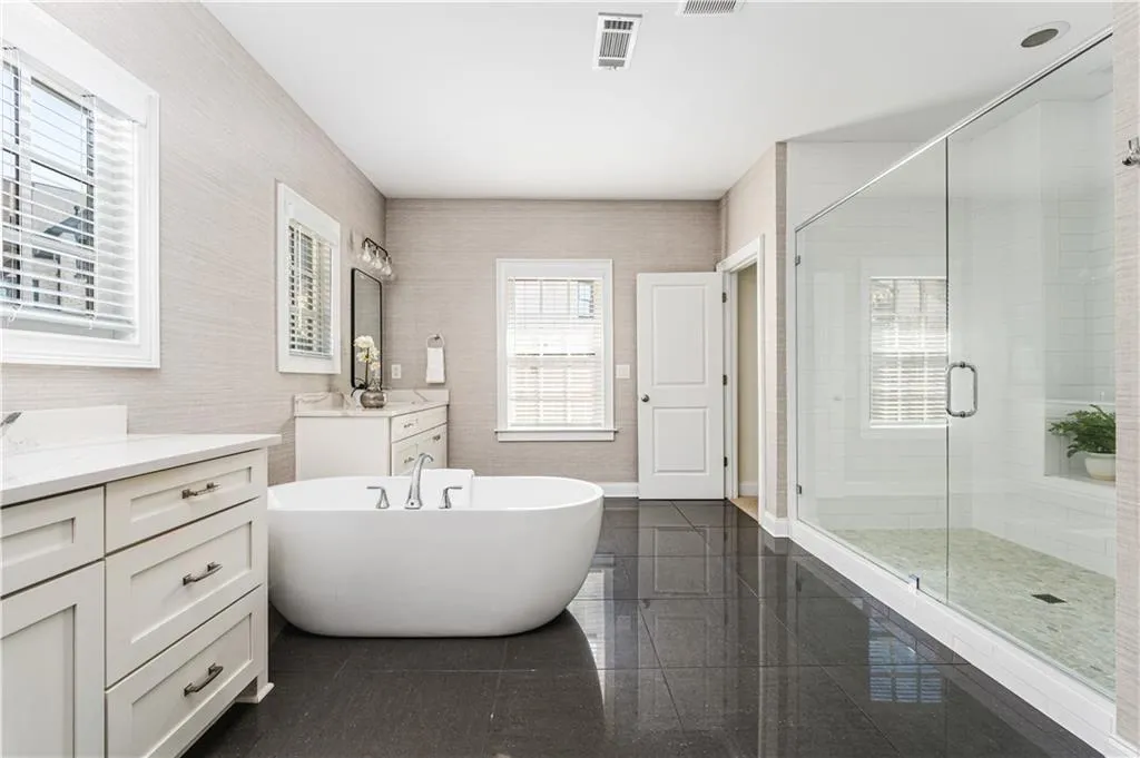 Full bath with tile walls, a soaking tub, two vanities, visible vents, and a stall shower