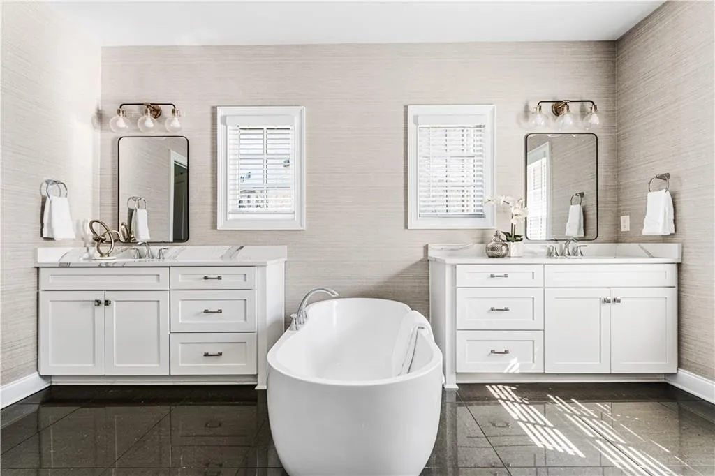 Bathroom with granite finish floor, a sink, two vanities, baseboards, and a soaking tub