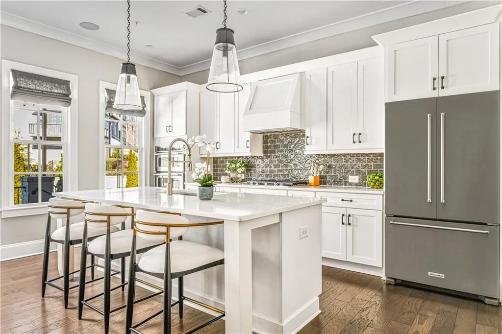 Kitchen with stainless steel appliances, custom range hood, visible vents, ornamental molding, and an island with sink