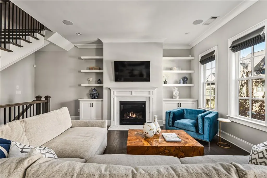 Living room with built in features, baseboards, a fireplace with flush hearth, ornamental molding, and wood finished floors