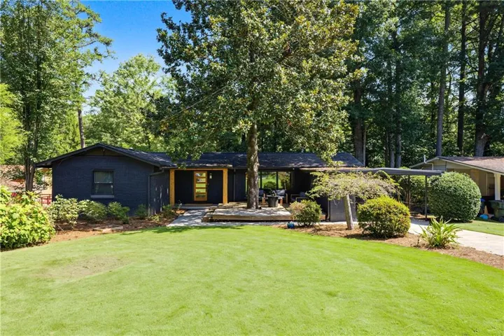 Contemporary exterior with dark siding, a wooden entry deck, a front lawn, and mature trees