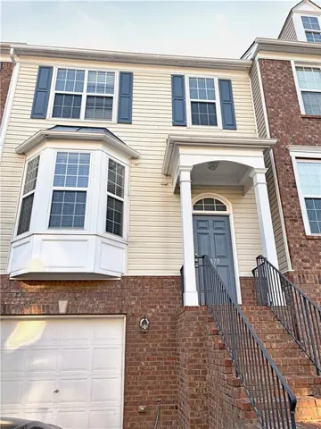 Brick and siding exterior featuring a covered entry, bay window, white garage door, and black metal railings