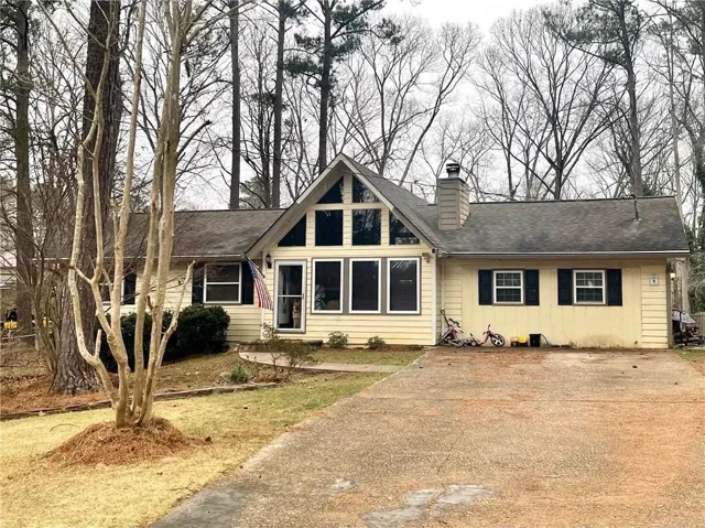 Siding exterior, gabled roofline, prominent chimney, mature trees, and a paved driveway