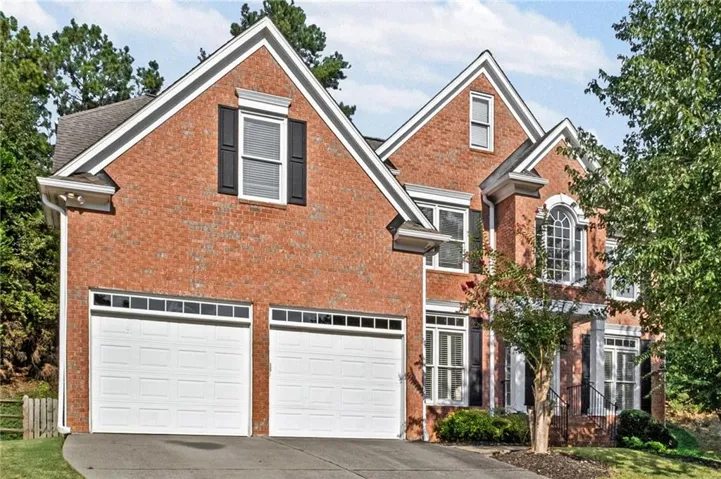 Brick exterior with gabled roof lines, white garage doors with window inserts, arched window detailing, and decorative black shutters