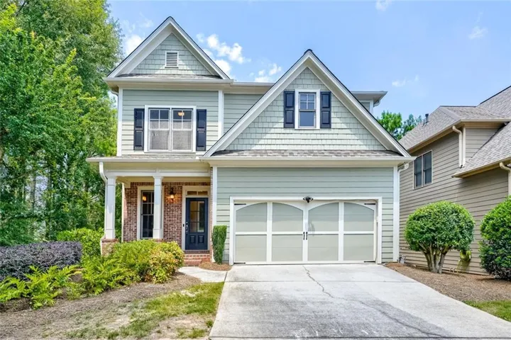 Craftsman-style home featuring light green siding, decorative shingle gables, and a two-car garage with arched paneling