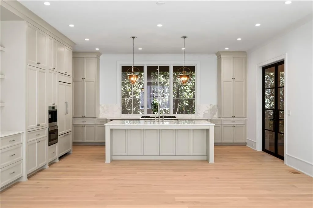 Hardwood flooring extends throughout this kitchen featuring a large central island, integrated appliances, recessed lighting, and a black-framed glass door