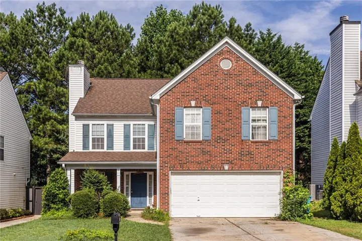 Traditional two-story residence featuring a brick and siding facade, an attached two-car garage, a covered front porch, and mature landscaping