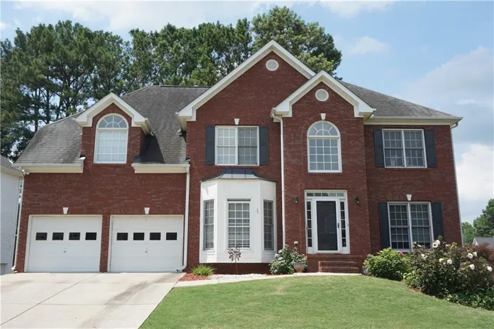 Brick facade residence with a two-car garage, manicured lawn, and mature landscaping