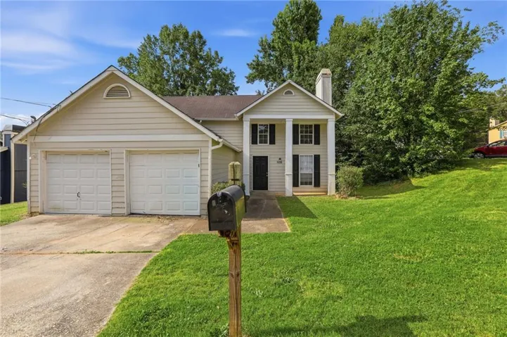 Traditional-style residence featuring a two-car garage, mature landscaping, and a columned entry