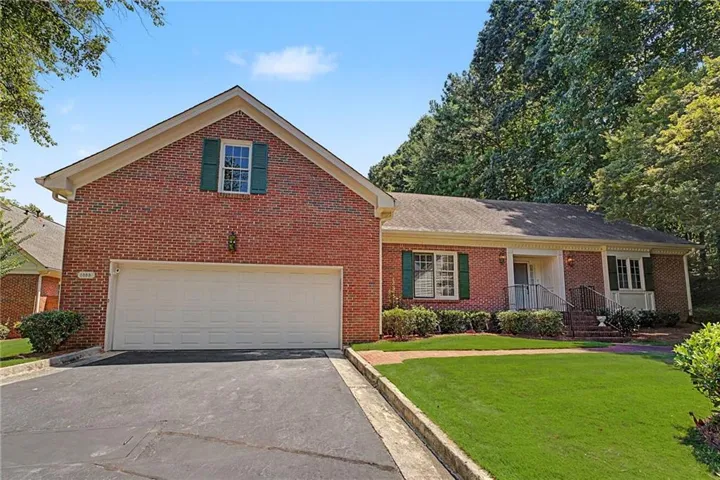 Brick facade with a two-car garage, mature landscaping, and an inviting front entry with a portico