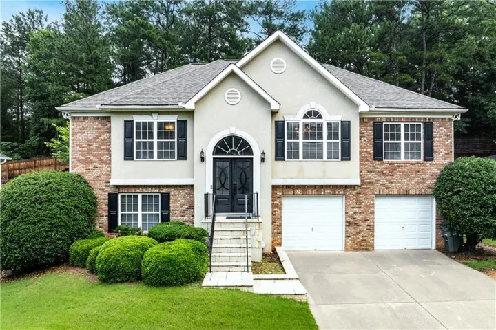 Two-story stucco and brick exterior featuring a prominent arched entry with double doors, symmetrical front windows with shutters, and a two-car garage