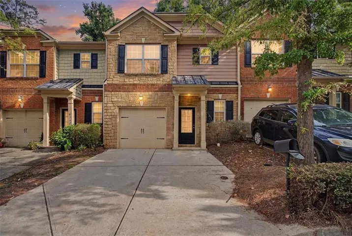 Stone and brick facade with black window shutters, a covered entry, and an attached garage