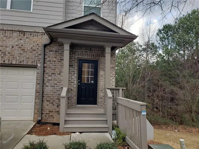 Welcoming front entry features a brick exterior with a covered portico, black paneled door with sidelights, white columns, and composite decking