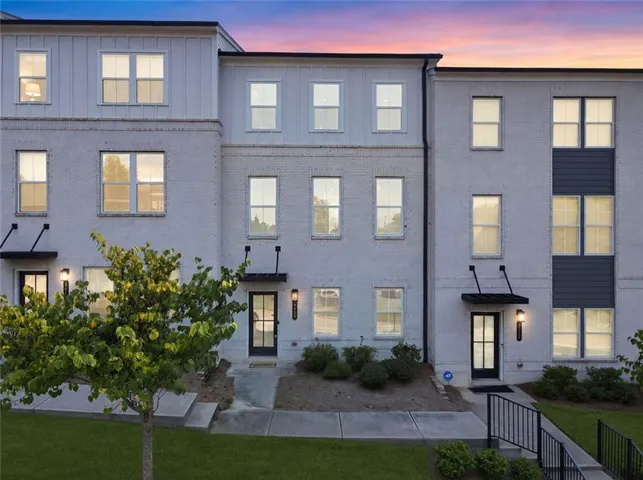 Brick exterior with board and batten accents, multiple windows, front entry doors with transom panels, and outdoor lighting fixtures
