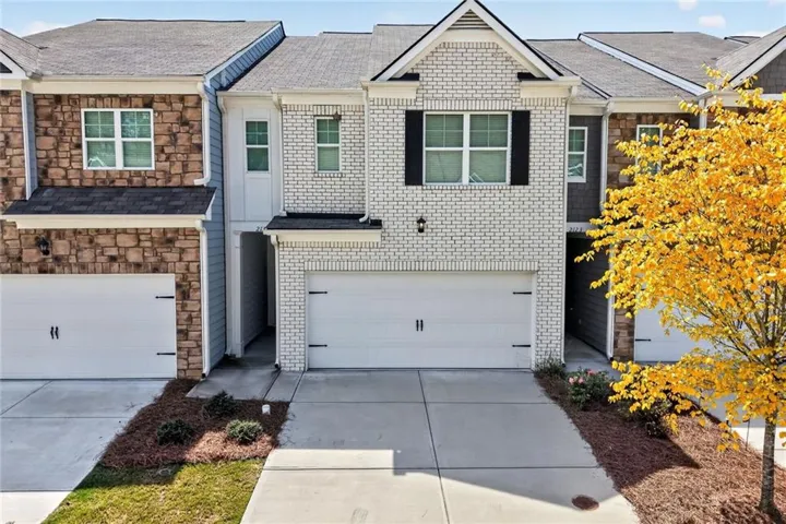 White brick exterior, integrated garage, concrete driveway, dark shutters, and a gabled roofline