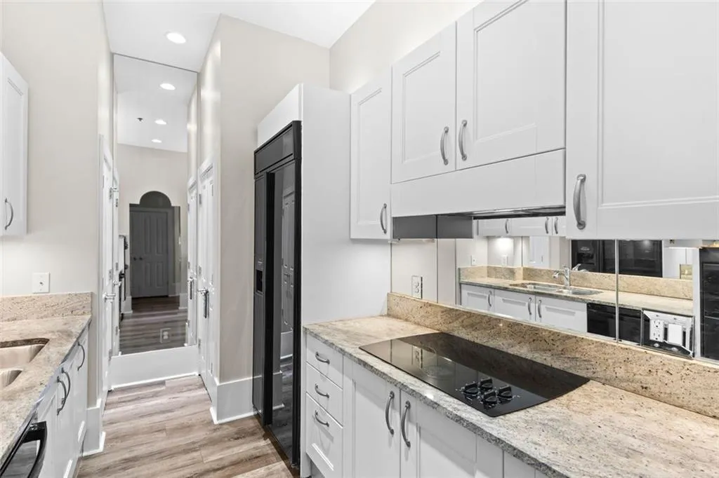 Galley kitchen has white cabinets and stone countertops