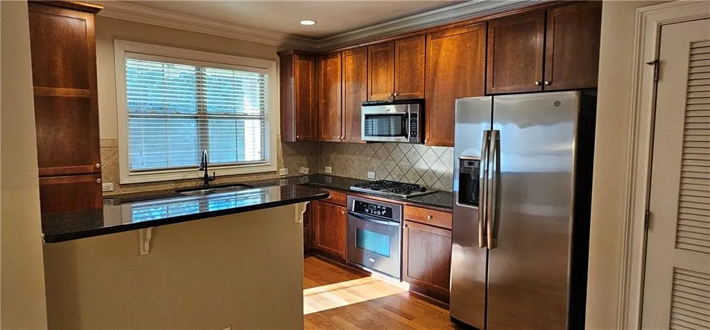 Kitchen with appliances with stainless steel finishes, ornamental molding, backsplash, light wood-style flooring, and a breakfast bar