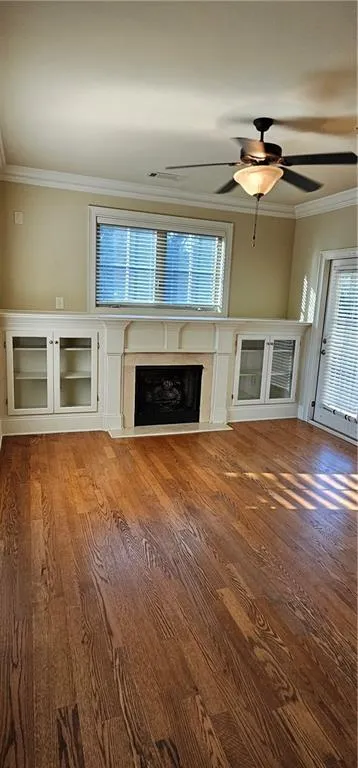Living room with a premium fireplace, crown molding, ceiling fan, and wood finished floors