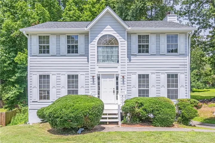 Two-story facade featuring light-colored siding, multiple windows with decorative shutters, a central arched window, and a prominent front entrance with white steps