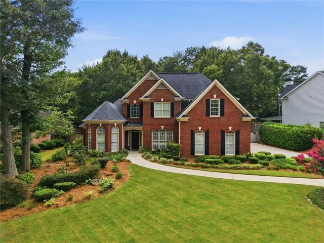 Traditional brick residence featuring a dark shingle roof, arched windows, and functional black shutters