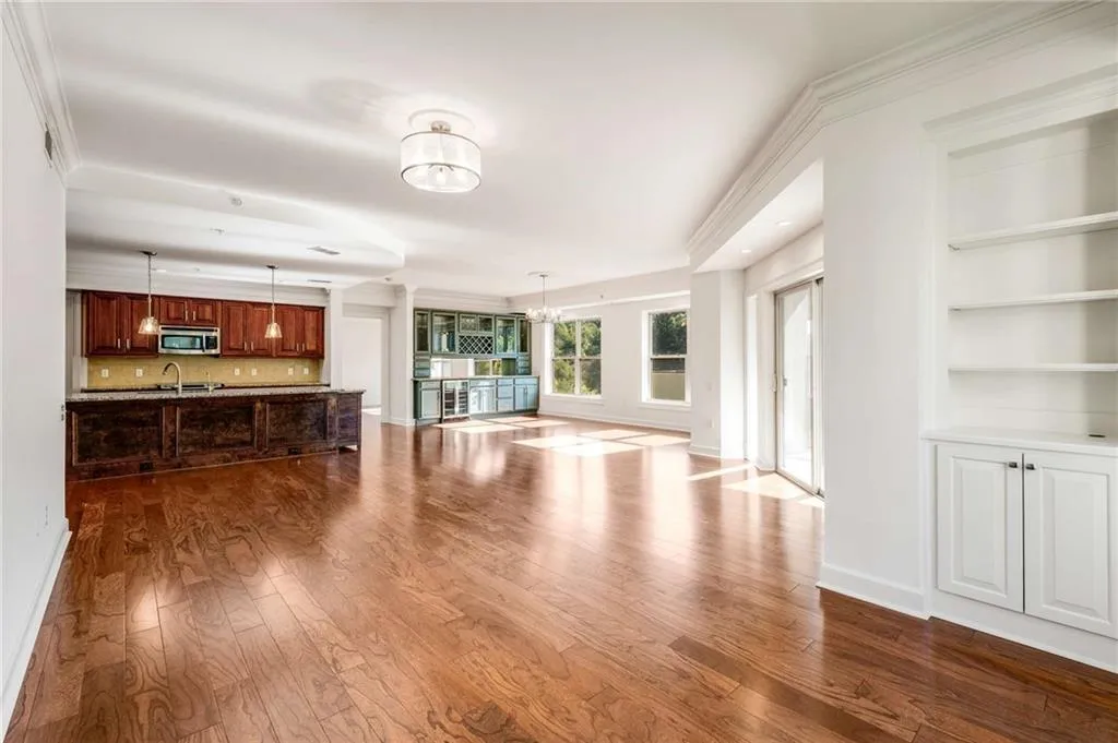 Unfurnished living room with wood-type flooring, crown molding, built in shelves, sink, and a chandelier