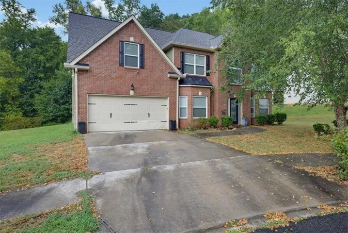 Brick facade residence with a two-car garage, multiple windows with dark shutters, and a front entry door