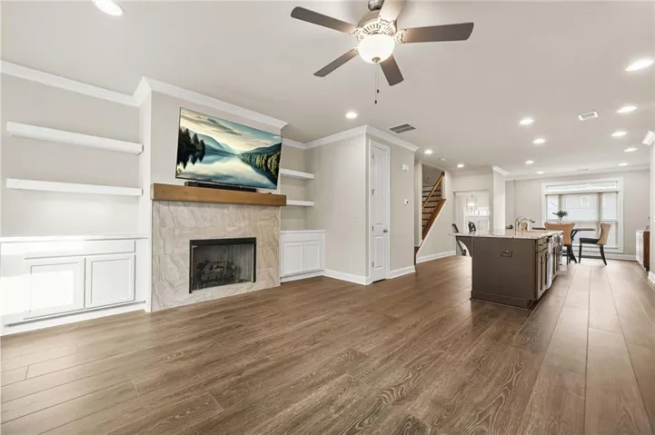 Living room with crown molding, dark wood-type flooring, a fireplace, recessed lighting, and stairs